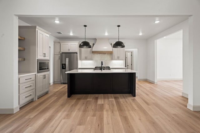 kitchen featuring pendant lighting, tasteful backsplash, stainless steel appliances, custom range hood, and a center island with sink