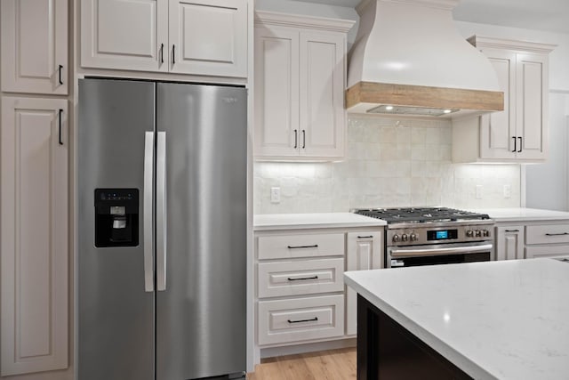 kitchen featuring appliances with stainless steel finishes, tasteful backsplash, white cabinetry, custom exhaust hood, and light stone counters