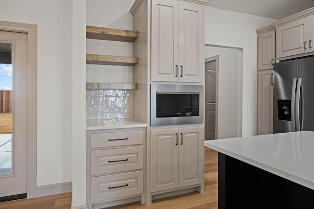 kitchen with built in microwave, stainless steel fridge, light hardwood / wood-style floors, and light stone counters