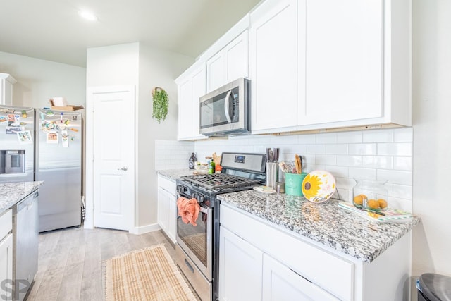 kitchen with appliances with stainless steel finishes, tasteful backsplash, white cabinetry, light stone countertops, and light wood-type flooring