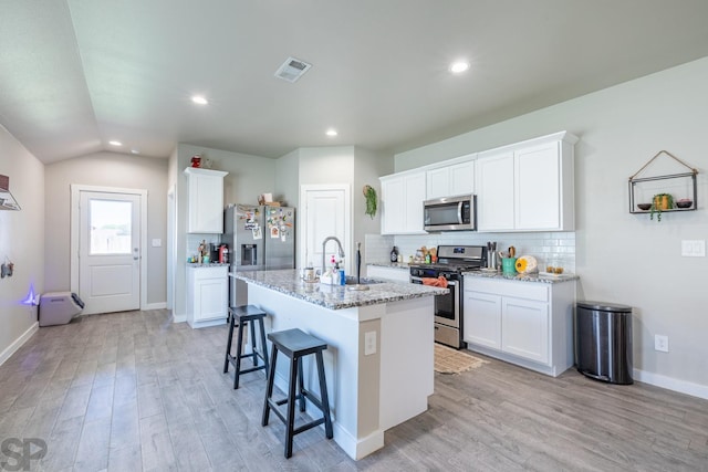 kitchen with light stone counters, white cabinetry, appliances with stainless steel finishes, and an island with sink