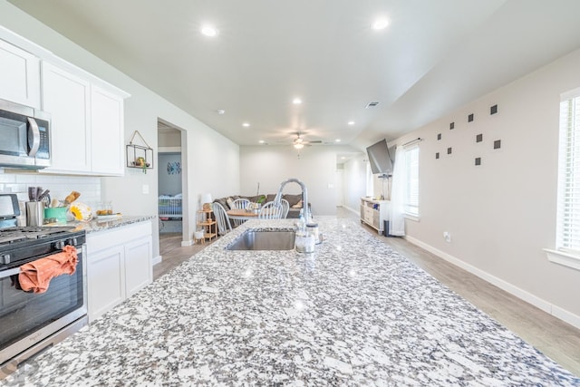 kitchen with white cabinetry, sink, backsplash, light stone counters, and stainless steel appliances