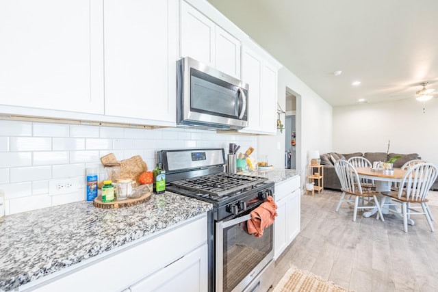 kitchen with white cabinetry, backsplash, stainless steel appliances, light stone countertops, and light hardwood / wood-style flooring