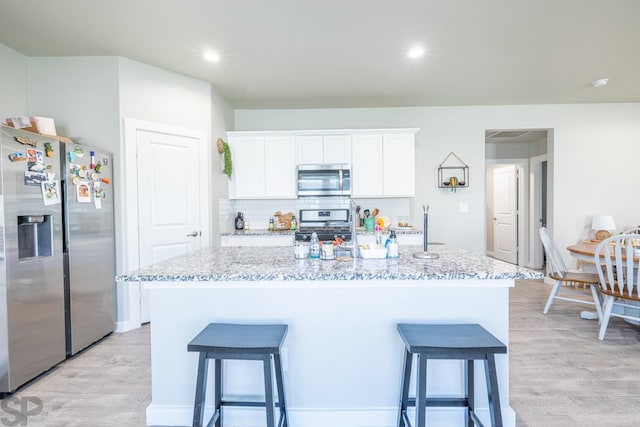 kitchen with appliances with stainless steel finishes, tasteful backsplash, light stone countertops, white cabinets, and a center island with sink