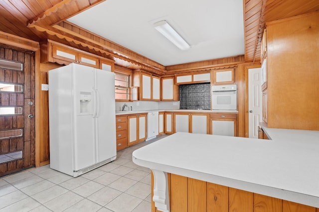 kitchen featuring wood walls, sink, light tile patterned floors, kitchen peninsula, and white appliances