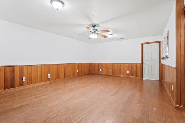 unfurnished room with wood-type flooring, ceiling fan, and wood walls