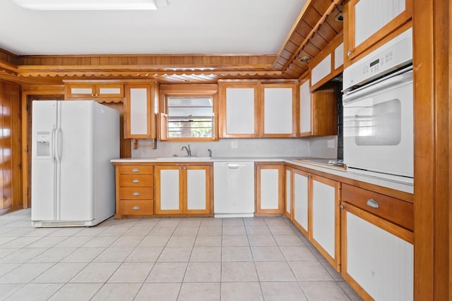 kitchen featuring sink, white appliances, wooden walls, and light tile patterned floors