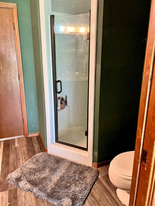 bathroom with wood-type flooring, a shower with door, and toilet