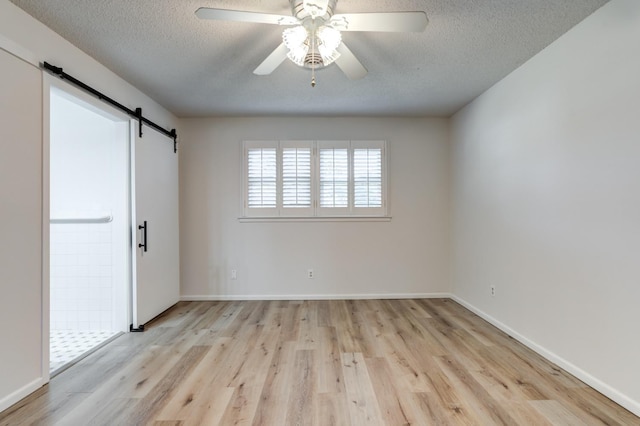 unfurnished bedroom featuring ceiling fan, a barn door, a textured ceiling, and light hardwood / wood-style flooring