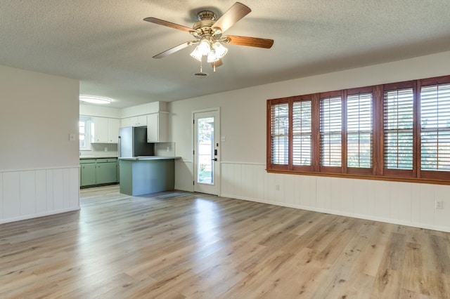 unfurnished living room featuring ceiling fan, a textured ceiling, and light hardwood / wood-style floors