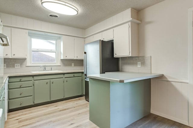 kitchen featuring sink, stainless steel fridge, green cabinets, light hardwood / wood-style floors, and white cabinets