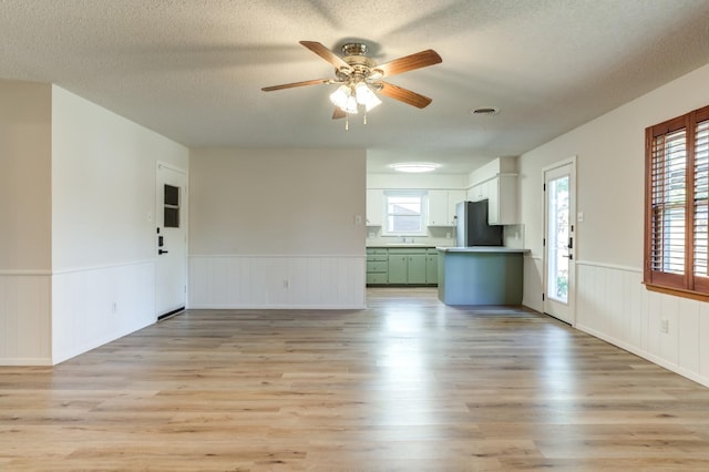 unfurnished living room with ceiling fan, sink, a textured ceiling, and light hardwood / wood-style flooring