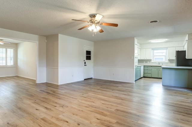 unfurnished living room with sink, a textured ceiling, ceiling fan, and light hardwood / wood-style flooring