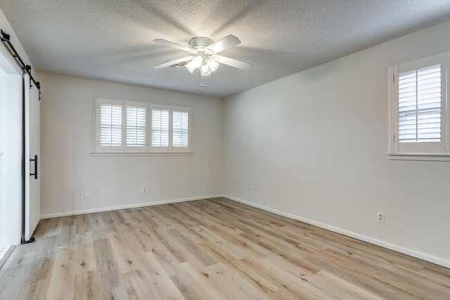 unfurnished room with a textured ceiling, a barn door, ceiling fan, and light wood-type flooring