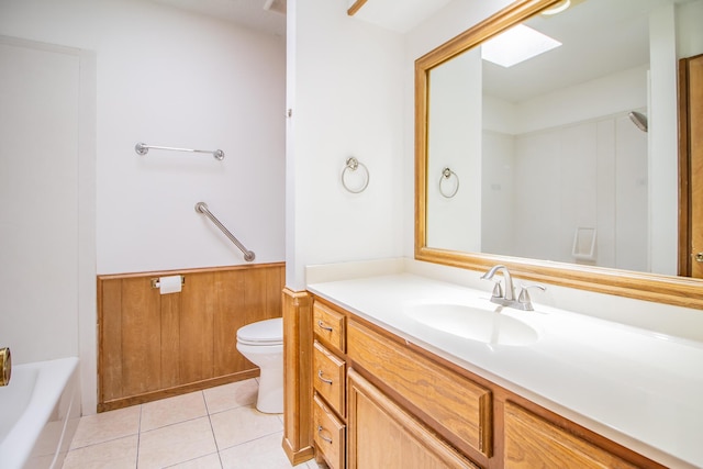 full bath featuring a tub to relax in, toilet, a wainscoted wall, vanity, and tile patterned floors