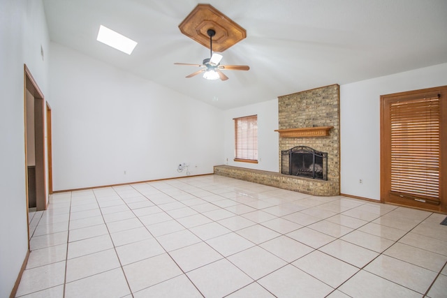 unfurnished living room with light tile patterned floors, a skylight, baseboards, a ceiling fan, and a brick fireplace