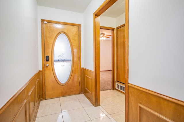 doorway to outside featuring light tile patterned floors, visible vents, wainscoting, ceiling fan, and a textured ceiling