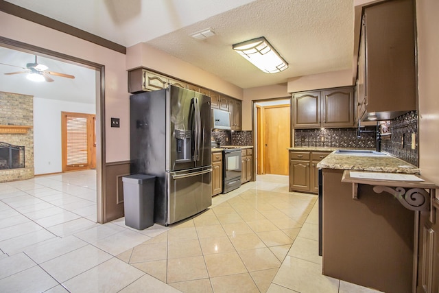 kitchen with light tile patterned floors, black range with electric stovetop, a fireplace, a sink, and stainless steel fridge