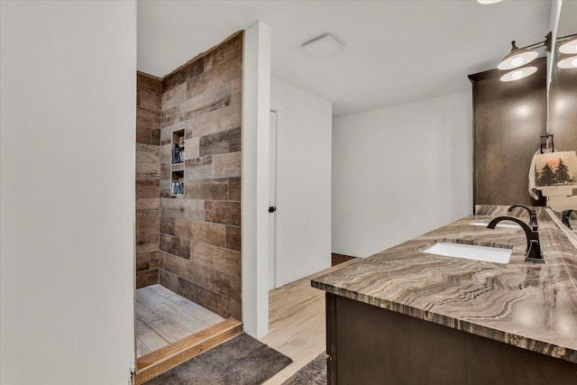 bathroom with a tile shower, vanity, and wood finished floors