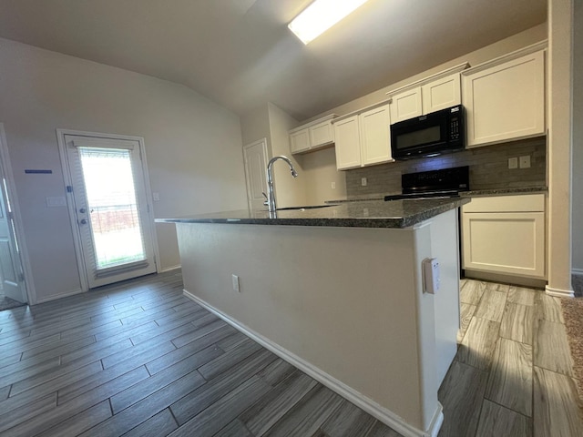 kitchen with white cabinetry, backsplash, lofted ceiling, and a center island with sink