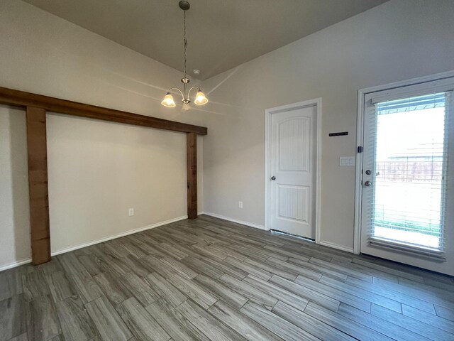 empty room with wood-type flooring, lofted ceiling, and an inviting chandelier