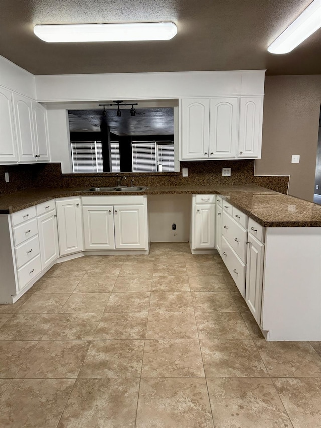 kitchen featuring sink, dark stone countertops, tasteful backsplash, white cabinets, and kitchen peninsula