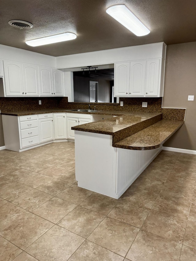 kitchen with a textured ceiling, dark stone countertops, kitchen peninsula, decorative backsplash, and white cabinets