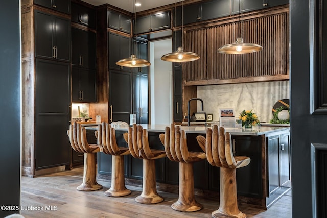 4510 Zadar Ave, Lubbock, TX 79407 - kitchen featuring light wood-style flooring, hanging light fixtures, a breakfast bar, tasteful backsplash, and a kitchen island with sink