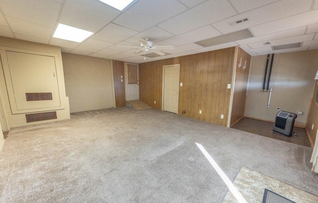 carpeted empty room featuring ceiling fan, a paneled ceiling, heating unit, and wood walls