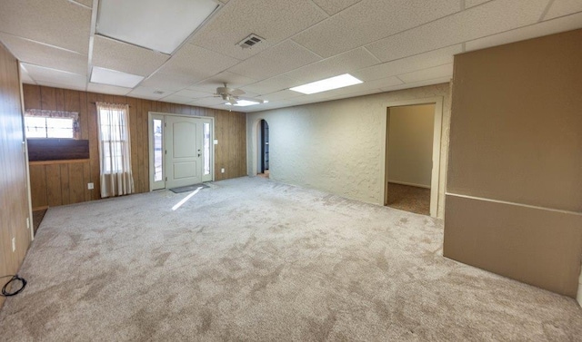 unfurnished room featuring carpet flooring, wooden walls, and ceiling fan