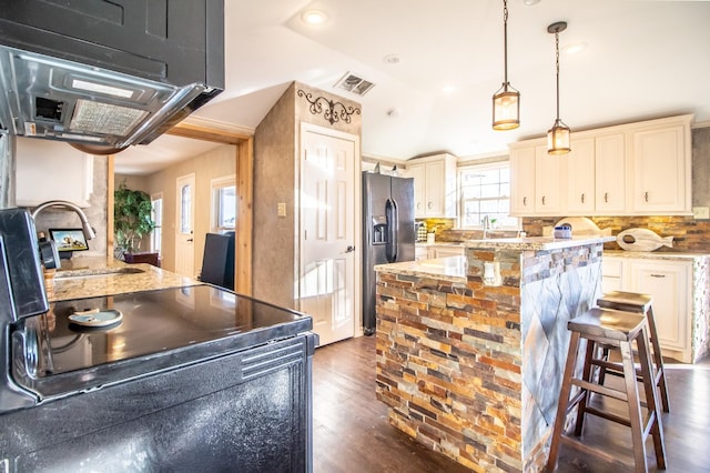 kitchen with electric stove, a breakfast bar area, hanging light fixtures, light stone counters, and stainless steel fridge with ice dispenser