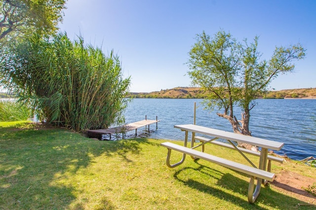 view of dock with a lawn and a water view