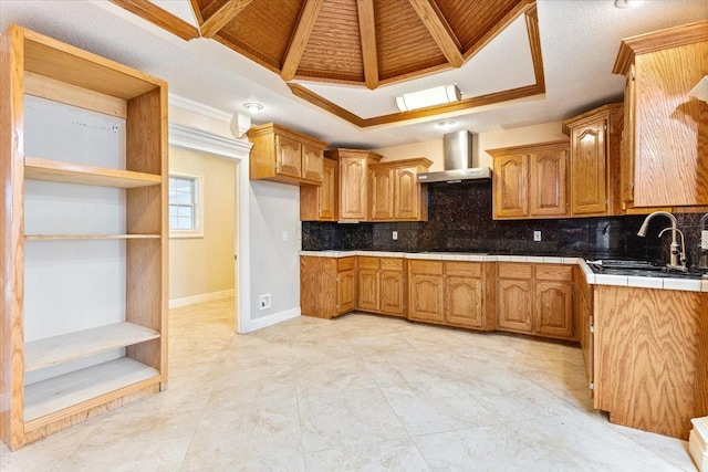 kitchen featuring sink, decorative backsplash, tile countertops, a raised ceiling, and wall chimney exhaust hood