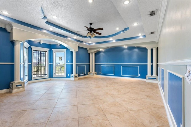 empty room with ornate columns, a textured ceiling, light tile patterned floors, a raised ceiling, and ceiling fan