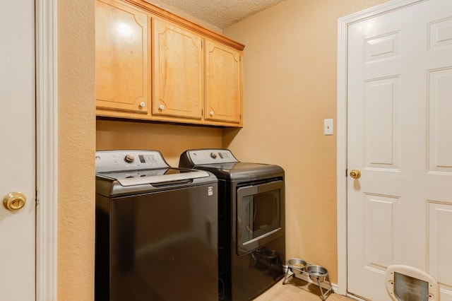 clothes washing area with cabinets, washing machine and clothes dryer, and a textured ceiling