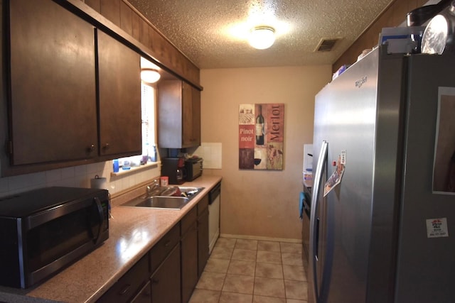 kitchen with sink, tasteful backsplash, a textured ceiling, light tile patterned floors, and stainless steel refrigerator