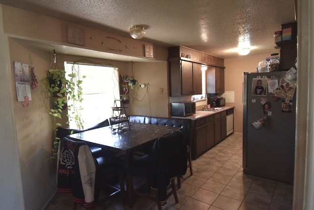 kitchen with light tile patterned flooring, sink, a textured ceiling, stainless steel fridge, and white dishwasher