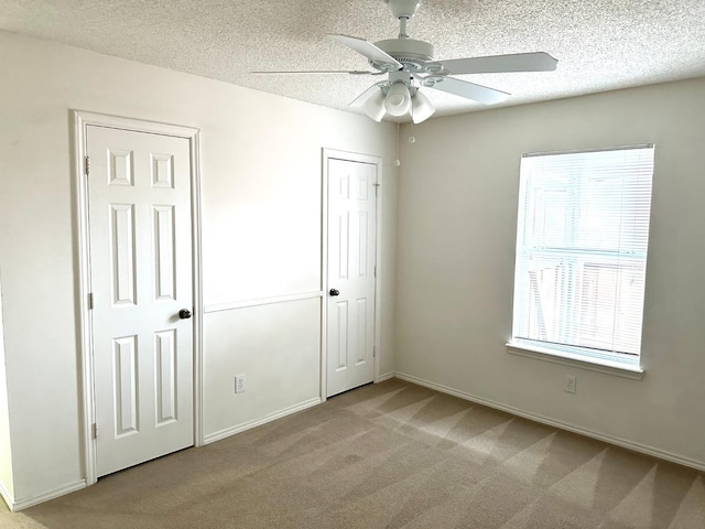 unfurnished bedroom featuring multiple windows, ceiling fan, light colored carpet, and a textured ceiling