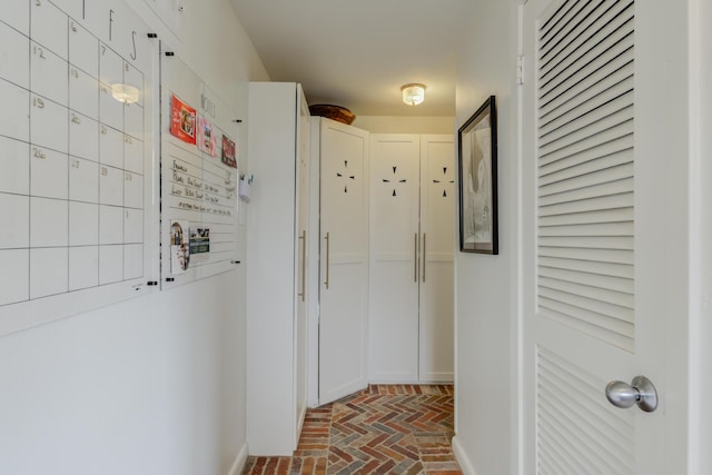 corridor featuring brick floor and baseboards