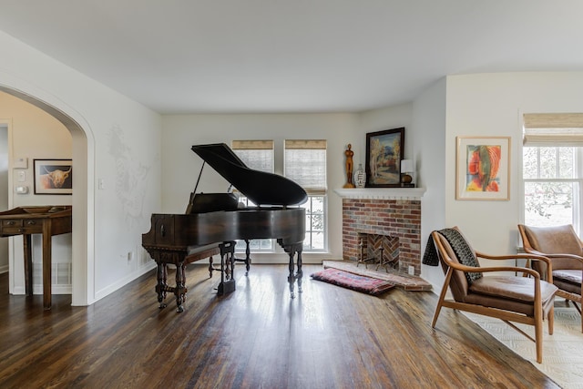 sitting room featuring arched walkways, wood finished floors, baseboards, and a brick fireplace