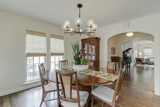 dining space featuring a chandelier, arched walkways, dark wood-style floors, and a healthy amount of sunlight