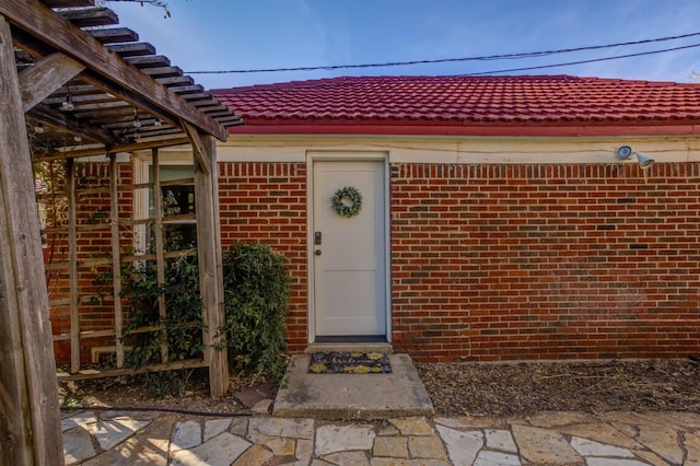 view of exterior entry featuring a tiled roof and brick siding