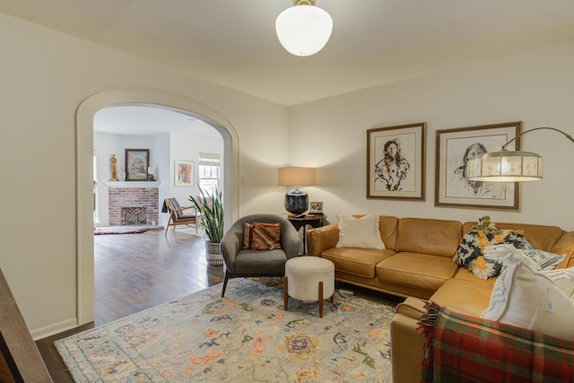 living area with baseboards, arched walkways, wood finished floors, and a fireplace