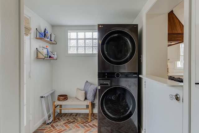 washroom with brick floor, stacked washing maching and dryer, and baseboards