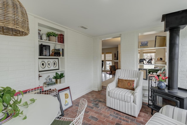 sitting room with brick floor, brick wall, a wood stove, and visible vents