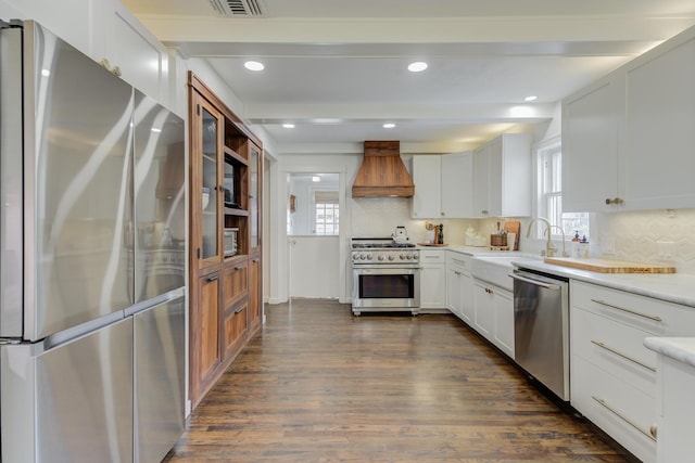 kitchen with tasteful backsplash, appliances with stainless steel finishes, light countertops, premium range hood, and dark wood-style floors