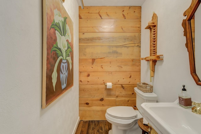 bathroom with toilet, wood finished floors, wooden walls, and a sink