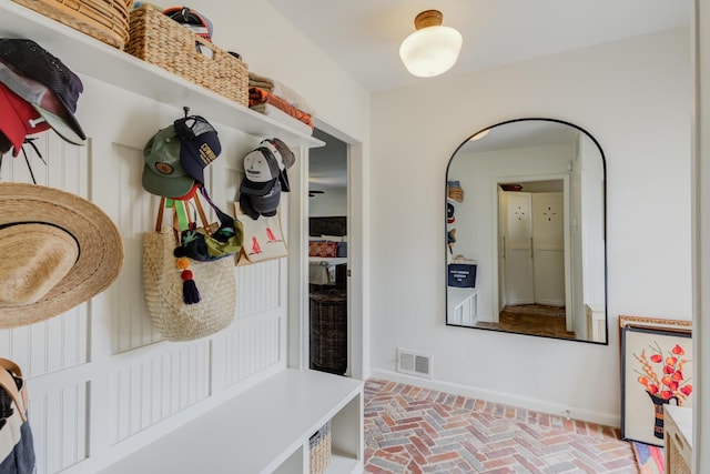 mudroom featuring visible vents, brick floor, and baseboards