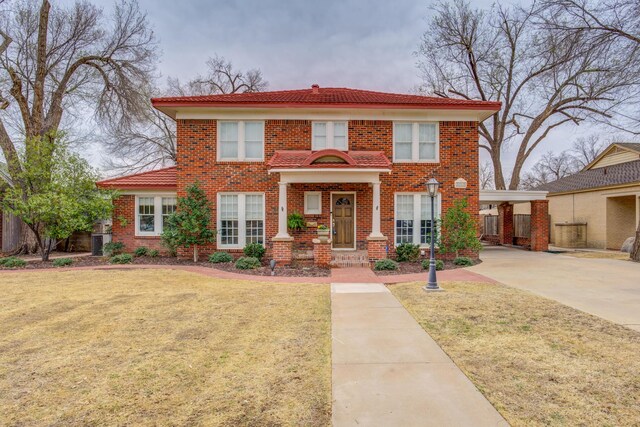 view of front facade with a front yard, a tile roof, brick siding, and a carport