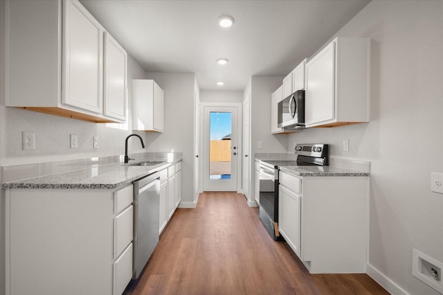 kitchen with sink, white cabinetry, light stone counters, wood-type flooring, and stainless steel appliances